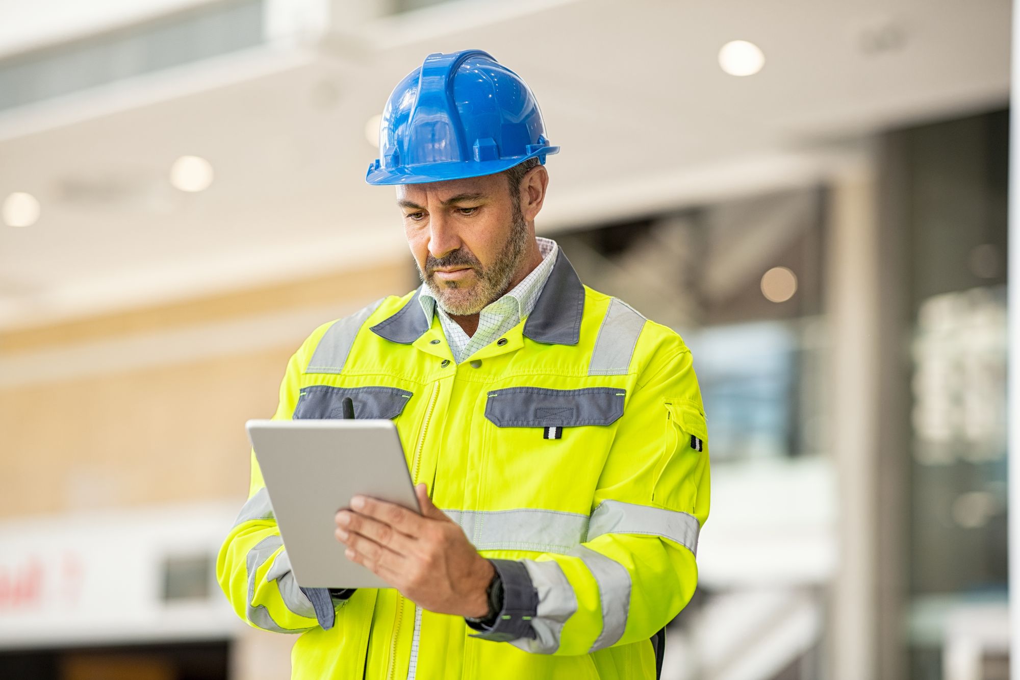 A worker in a high-visibility vest reading a tablet inside a building under construction