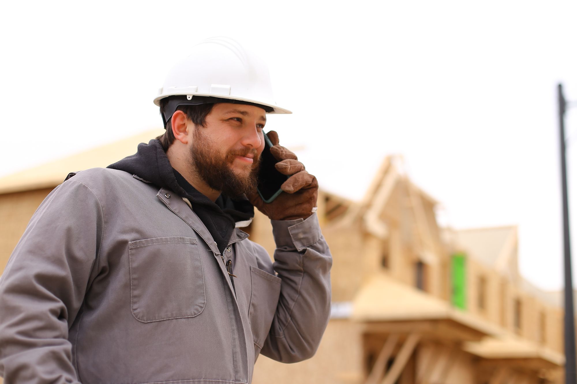 A subcontractor on the phone in front of a house being framed