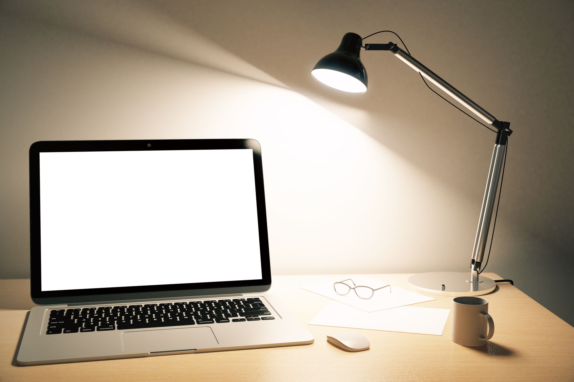 A laptop open under a desk lamp in the evening