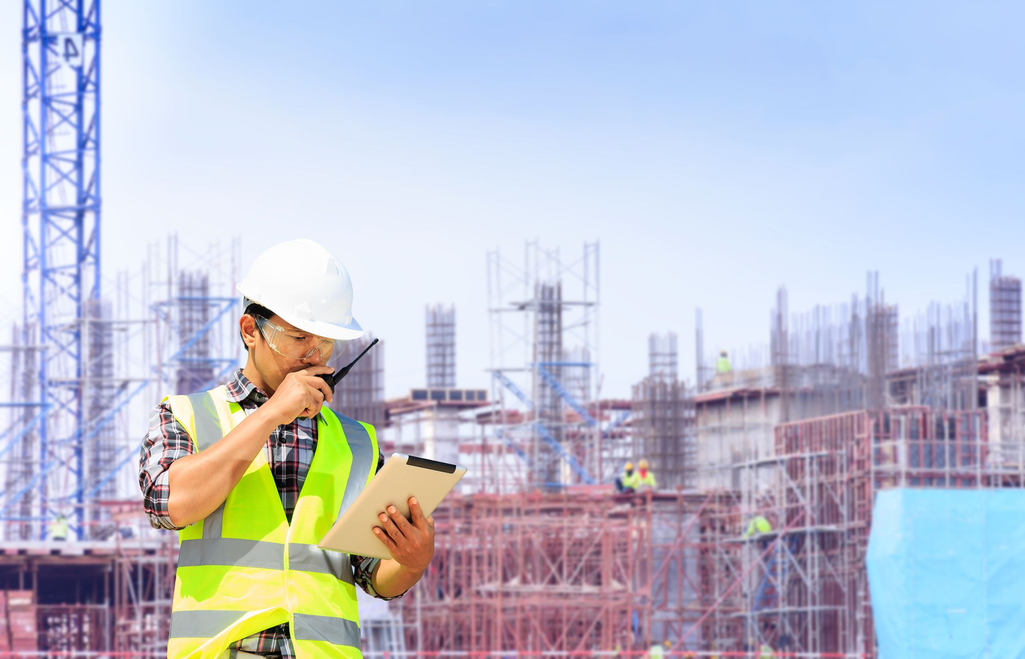 A superintendent with a tablet and a radio in front of a building under construction
