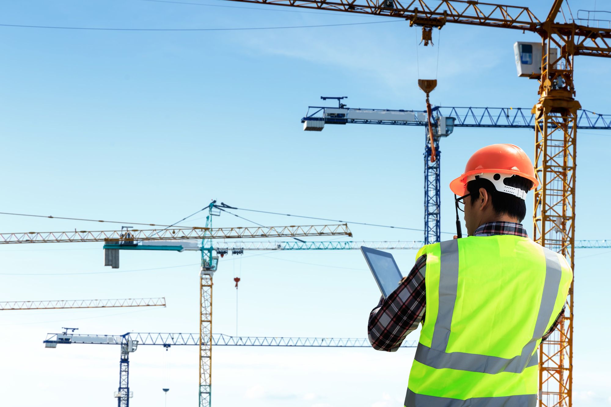 A worker with a tablet looking out over a site with tower cranes